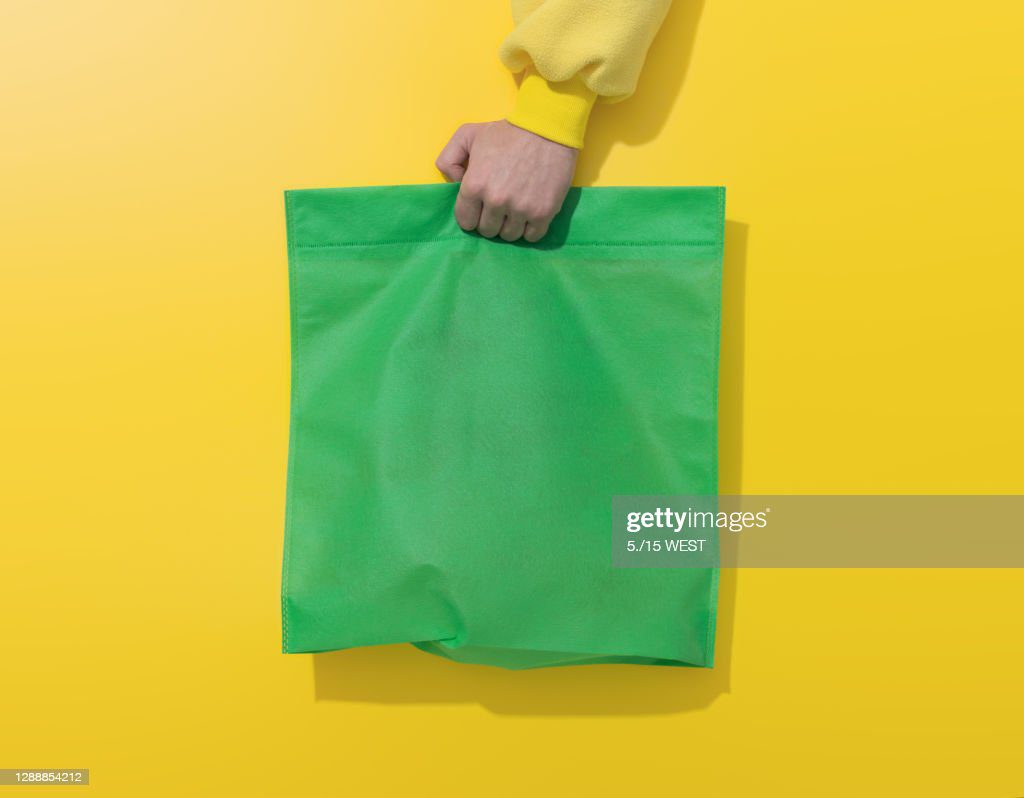 mano sostiene bolsa de algodón verde sobre fondo amarillo - bolsa vacia fotografías e imágenes de stock