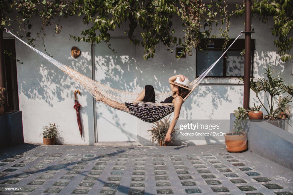 woman relaxing in hammock against wall at yard - hamaca fotografías e imágenes de stock