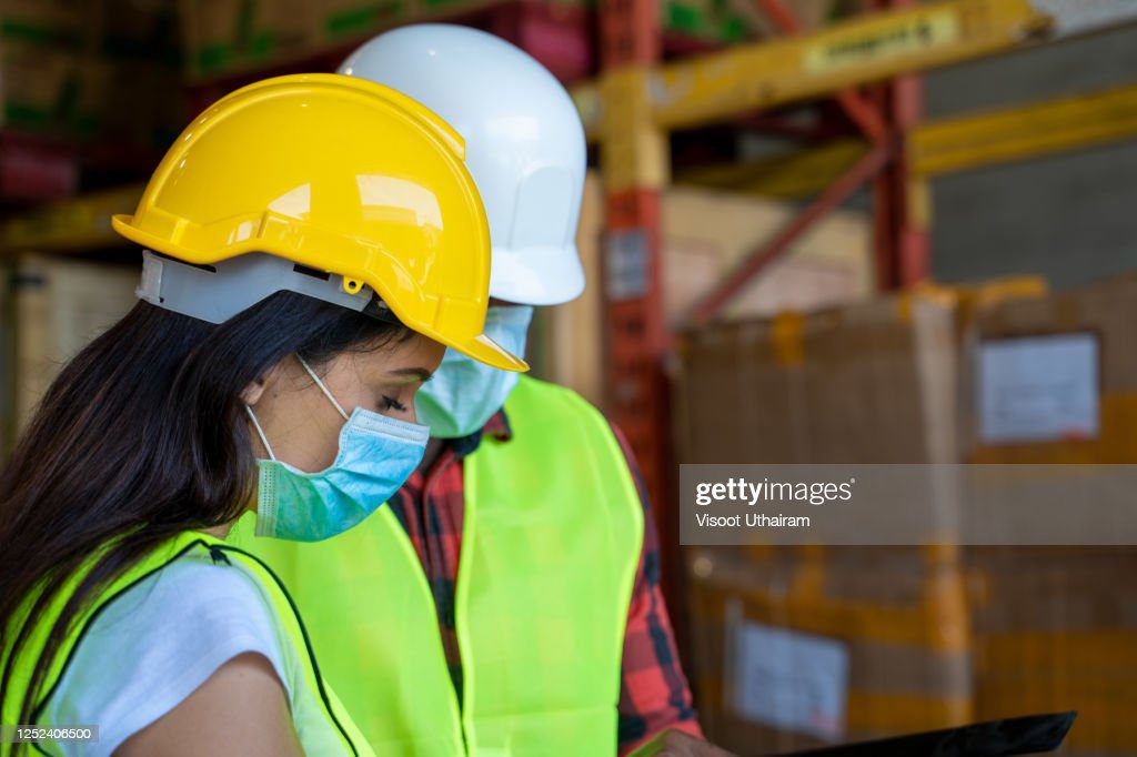 warehouse worker wearing protective mask to protect against covid-19 and checking production process - permiso de trabajo fotografías e imágenes de stock
