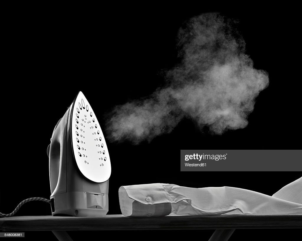 steaming flat iron and shirt sleeve in front of black background - plancha fotografías e imágenes de stock