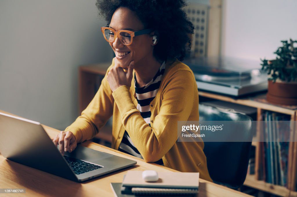 mujer afroamericana sonriente que lleva gafas y auriculares inalámbricos hace una videollamada en su computadora portátil en su oficina en casa - mujer negra fotografías e imágenes de stock