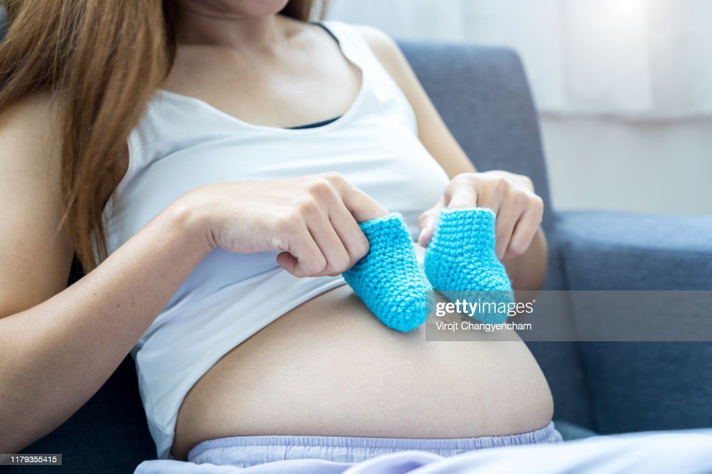 close up pregnant woman holding bump and tiny baby shoes on her tummy on the bed - embarazo adolescente fotografías e imágenes de stock