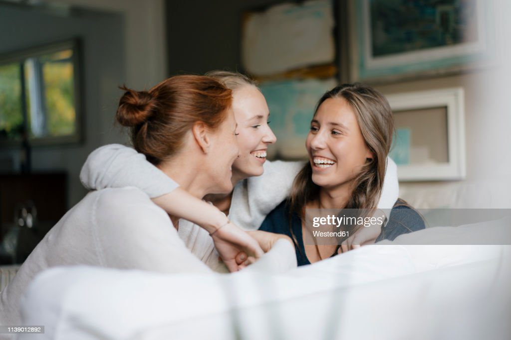 happy teenage girl hugging mother and sister on couch at home - hermana fotografías e imágenes de stock