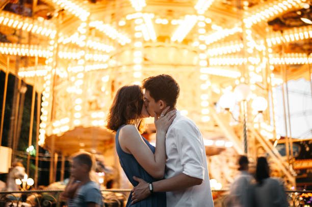 couple kissing near the marry-go-round in the park - beso fotografías e imágenes de stock