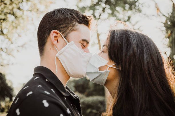 teenager couple kissing outdoors with protective facial mask - beso fotografías e imágenes de stock